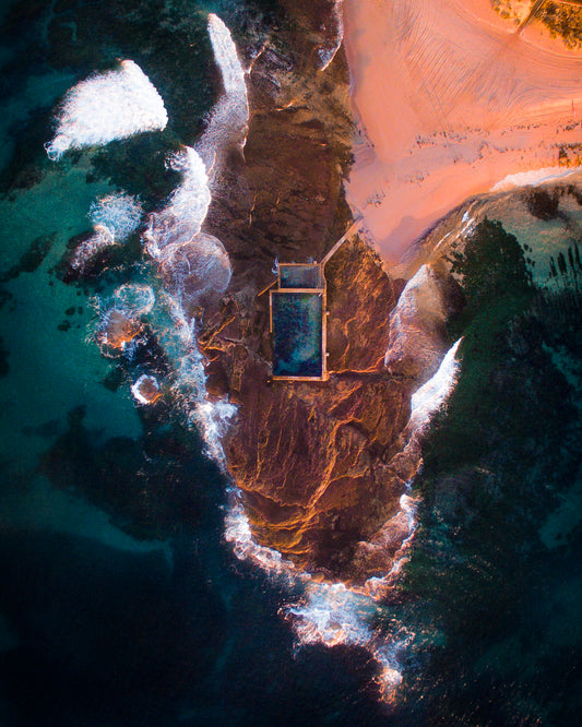 Cette photographie prise à New South Wales en Australie par le photographe Yorick Serriere grâce à un drone nous montre une piscine au bout d’une avancée rocheuse en bord de mer. La photographie est prise au coucher du soleil ce qui lui donne cette teinte rose orangée qui se mélange au bleu de l’océan et au blanc de l’écume des vagues.