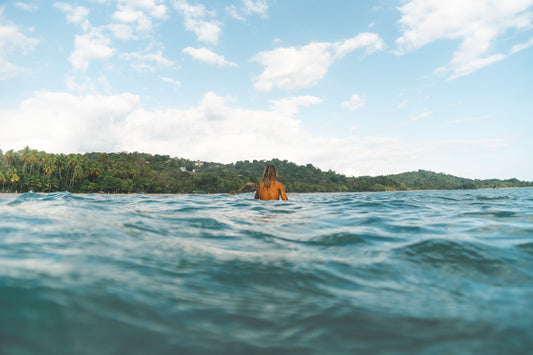 Cette photographie prise à Manuel Antonio au Costa Rica par le photographe Yorick Serriere nous montre un surfeur de dos attendant les vagues. La photographie est prise depuis l’eau avec comme point de vue le rivage remplit de palmiers. Le surfeur est au milieu de la photographie et la ligne d’horizon au milieu de la hauteur ce qui coupe la photo en 2.