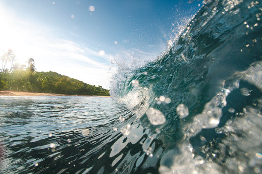 Cette photographie prise depuis l’intérieur d’une vague se situe à Manuel Antonio au Costa Rica. Elle a été prise par le photographe Yorick Serriere. Nous sommes au bord de la plage remplie de palmiers. Nous voyons au centre de la photographie le tube de la vague et en premier plan les gouttes qui sont sur l’objectif de l’appareil photo.