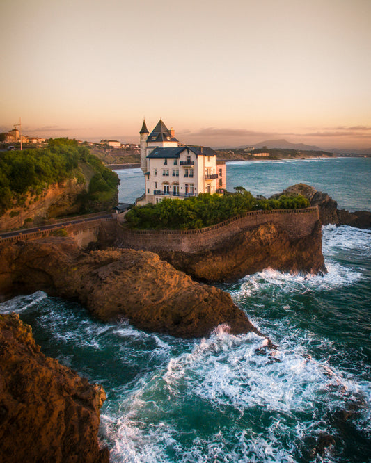 Cette photographie de la célèbre Villa Bella a été prise à Biarritz en France par le photographe Yorick Serriere en 2018. Cette photo est prise par un drone au dessus de la mer. Au premier plan nous voyons l’océan avec des vagues, au milieu se dresse la belle villa Belza et en arrière plan se trouvent les montagnes des Pyrénées dont la Rhune.