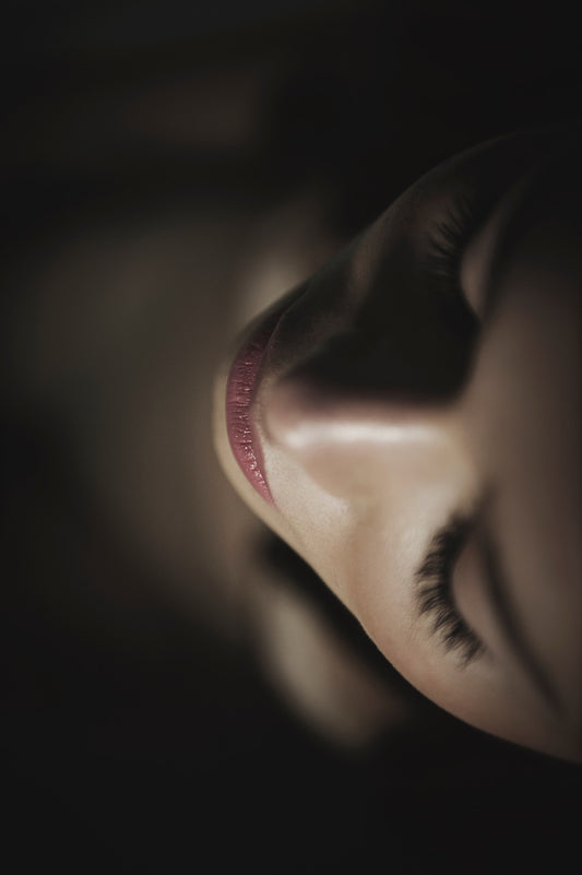 Portrait très rapproché d’une femme. Ses yeux sont fermés. Elle porte un léger rouge à lèvres. Cette photographie est réalisée par Vanessa Moselle.