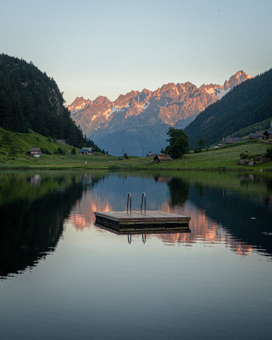 Cette photographie prise en Suisse par Yorick Serriere nous montre en lac de montagne. Au premier plan se trouve le lac d’un bleu profond où se reflète les montagnes situées en arrière plan. Le soleil couchant sur les montagnes leurs donnent une couleur rose orangée.